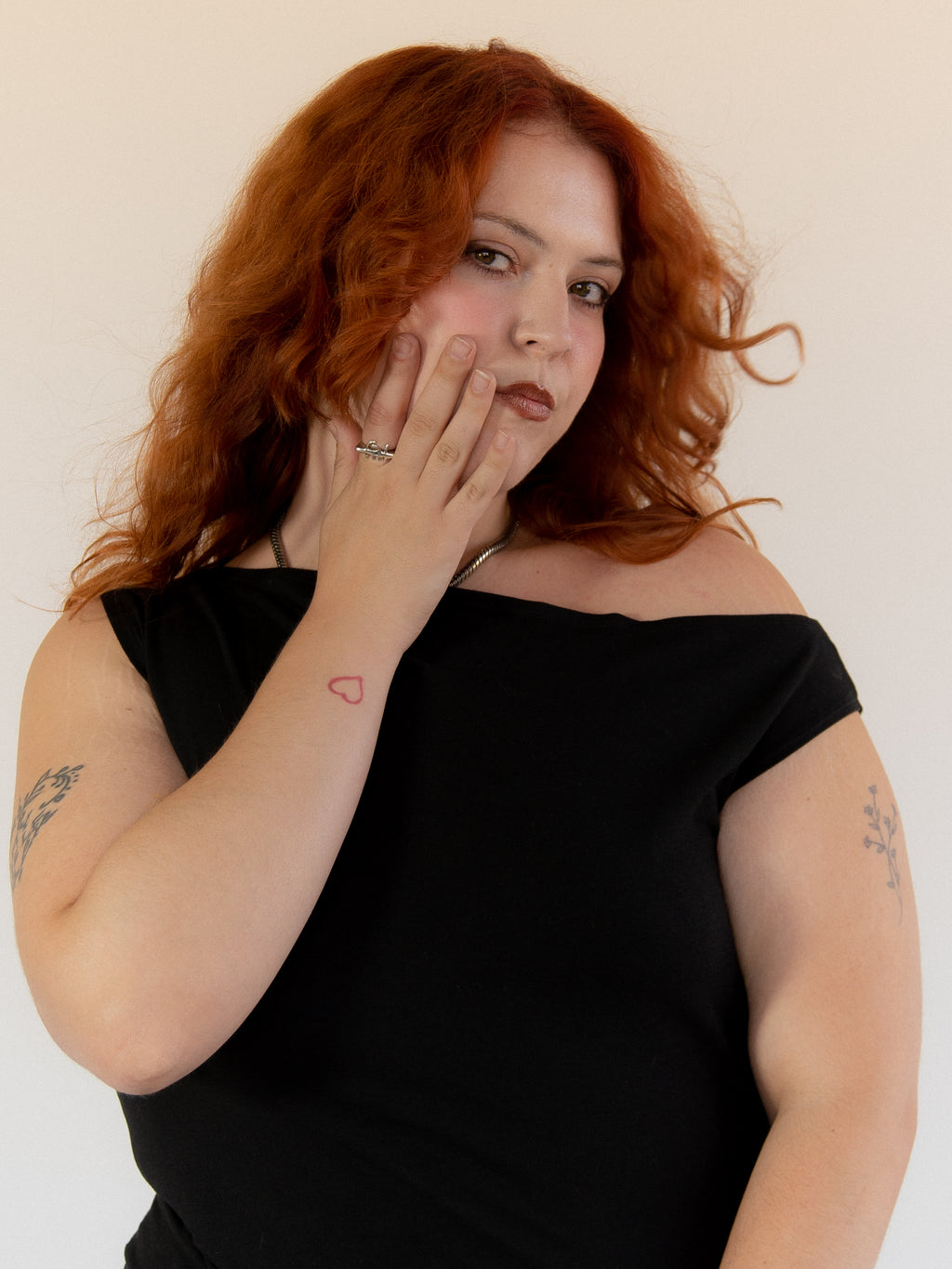Woman with red hair wearing a black off-shoulder top against a plain background